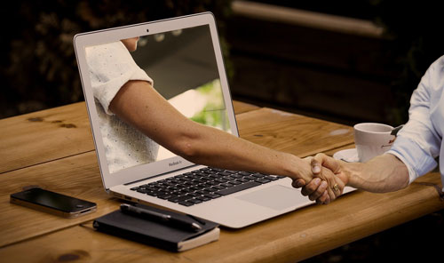 A handshake reaching out of a laptop screen