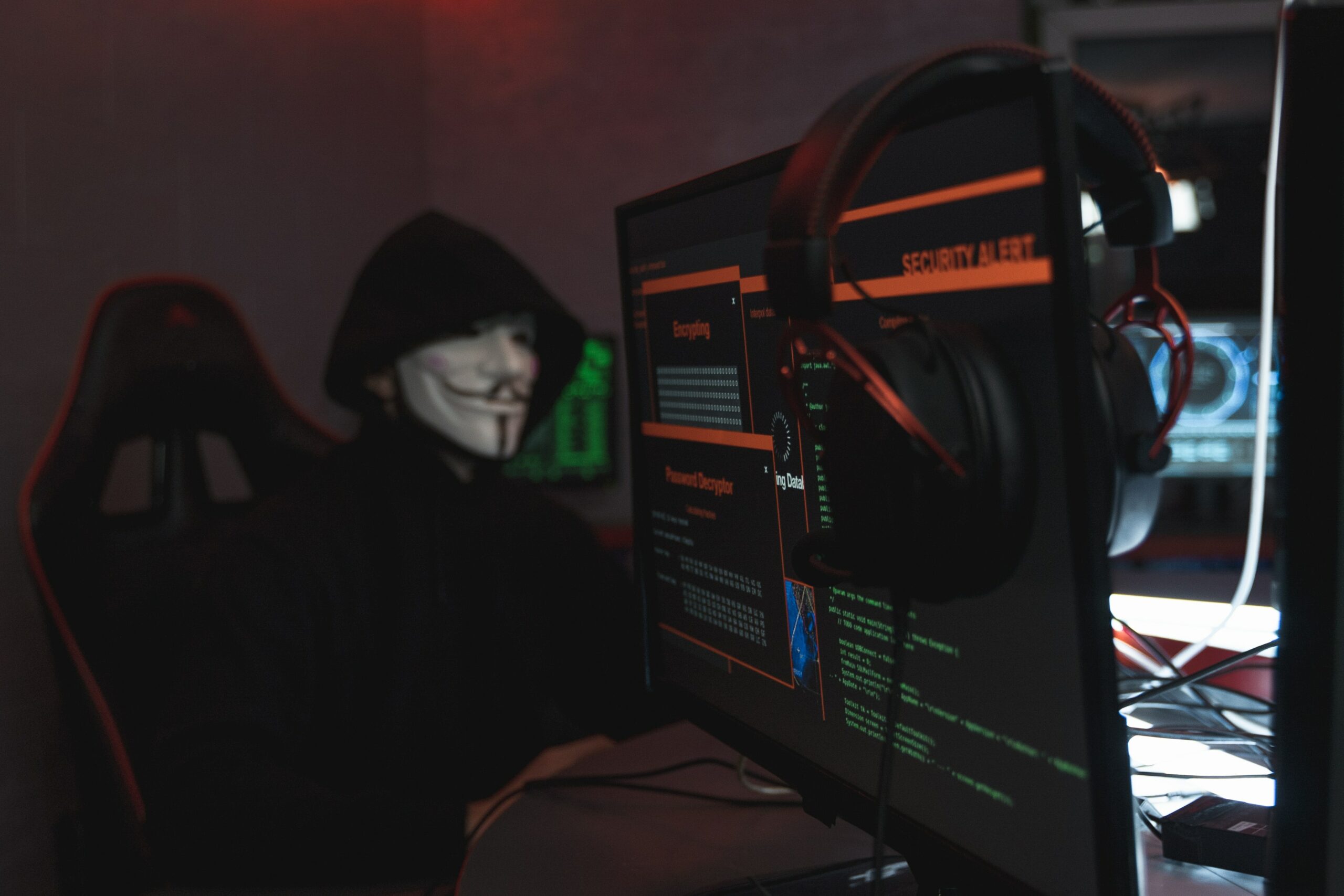 Shady character in a mask sitting by computer screens